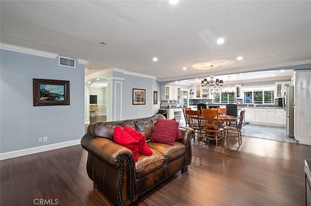 living area featuring crown molding, dark wood-type flooring, visible vents, and ornate columns