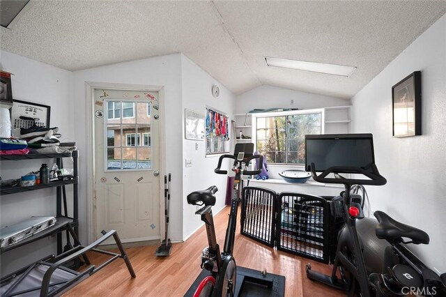 workout area with vaulted ceiling, a textured ceiling, wood finished floors, and a healthy amount of sunlight