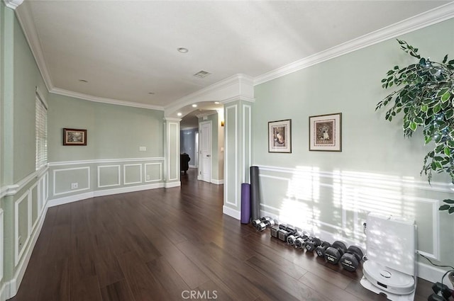 unfurnished room with arched walkways, wood finished floors, crown molding, ornate columns, and a decorative wall