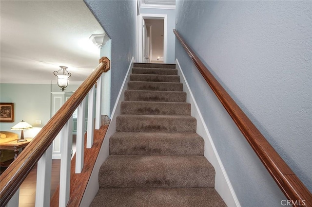 stairs featuring crown molding, wood finished floors, and a textured wall