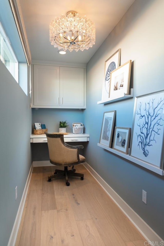 office with baseboards, built in desk, a chandelier, and light wood-style floors