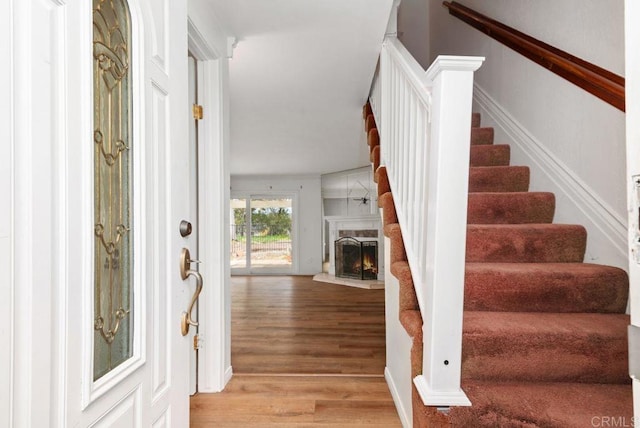 entrance foyer featuring light wood finished floors, a warm lit fireplace, and stairway