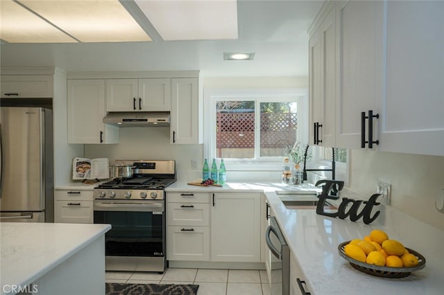 kitchen featuring light tile patterned floors, stainless steel appliances, white cabinetry, a sink, and under cabinet range hood