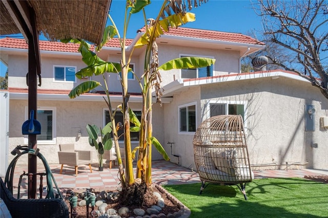 back of property featuring stucco siding, a tiled roof, a lawn, and a patio