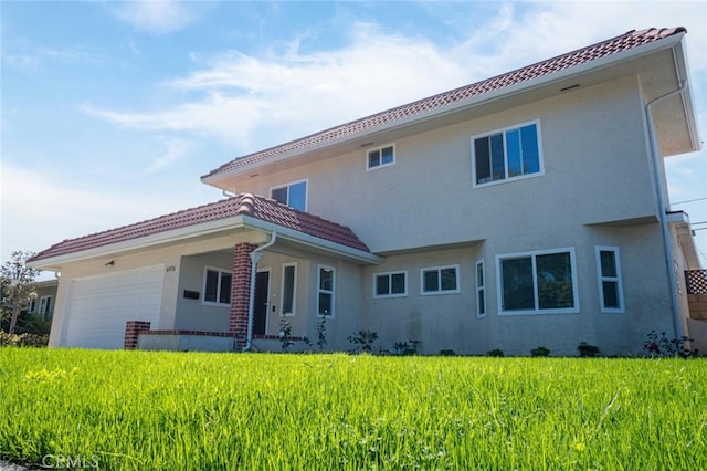 back of house featuring a garage, a tiled roof, a lawn, and stucco siding