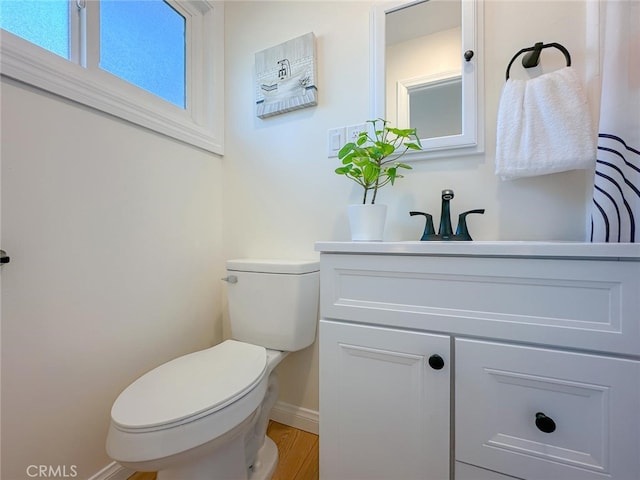 half bathroom with baseboards, vanity, and toilet