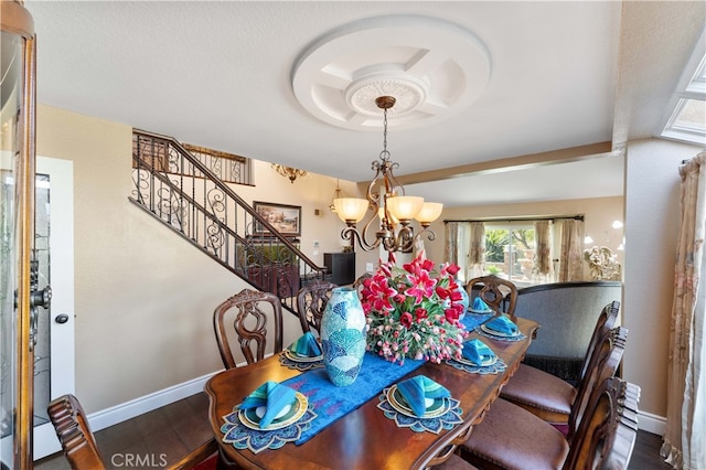 dining room with a notable chandelier, a raised ceiling, wood finished floors, baseboards, and stairs