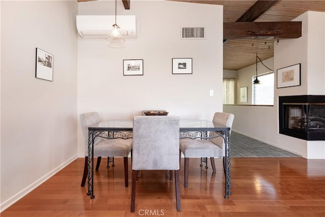 dining area with beam ceiling, visible vents, an AC wall unit, wood finished floors, and a multi sided fireplace