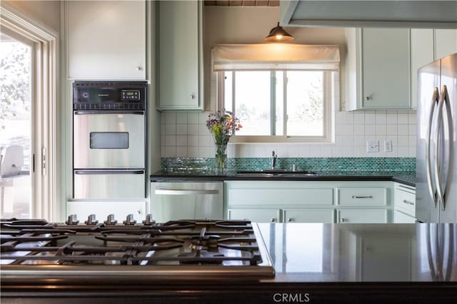 kitchen featuring appliances with stainless steel finishes, dark countertops, a sink, and decorative backsplash