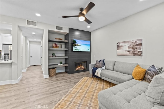 living area with light wood-type flooring, a large fireplace, visible vents, and baseboards