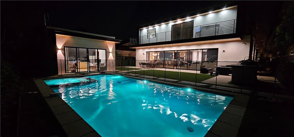 pool at night featuring a patio, a yard, fence, and a pool with connected hot tub