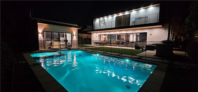 pool at night featuring a patio, a yard, fence, and a pool with connected hot tub