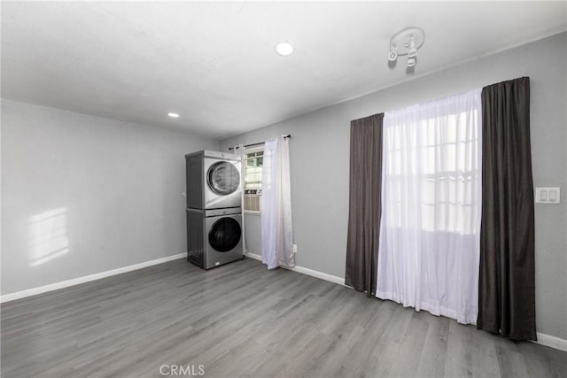 clothes washing area with stacked washer and clothes dryer, recessed lighting, wood finished floors, laundry area, and baseboards