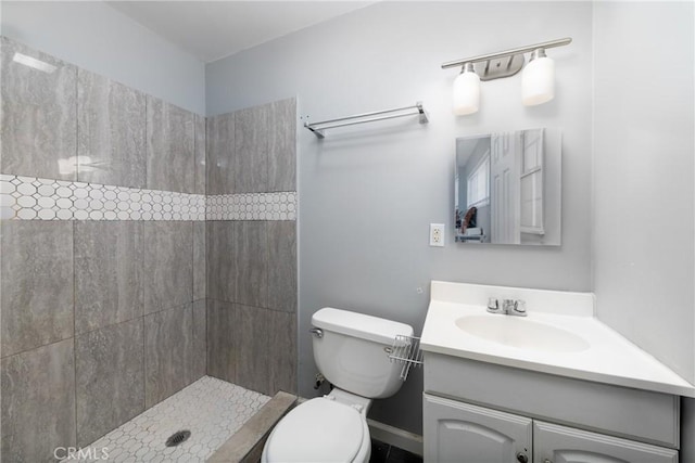 bathroom featuring toilet, tiled shower, and vanity