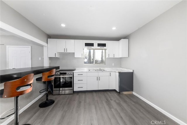 kitchen featuring electric range, light wood-type flooring, white cabinetry, and baseboards