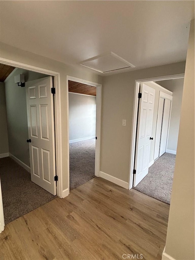 hall featuring attic access, carpet flooring, baseboards, and wood finished floors