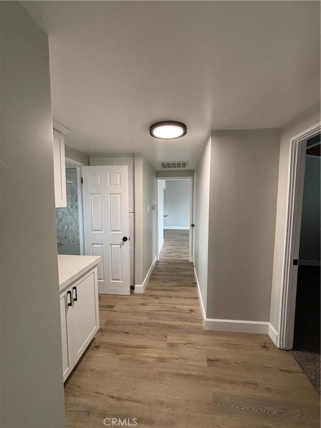 hall featuring light wood-type flooring, baseboards, and visible vents