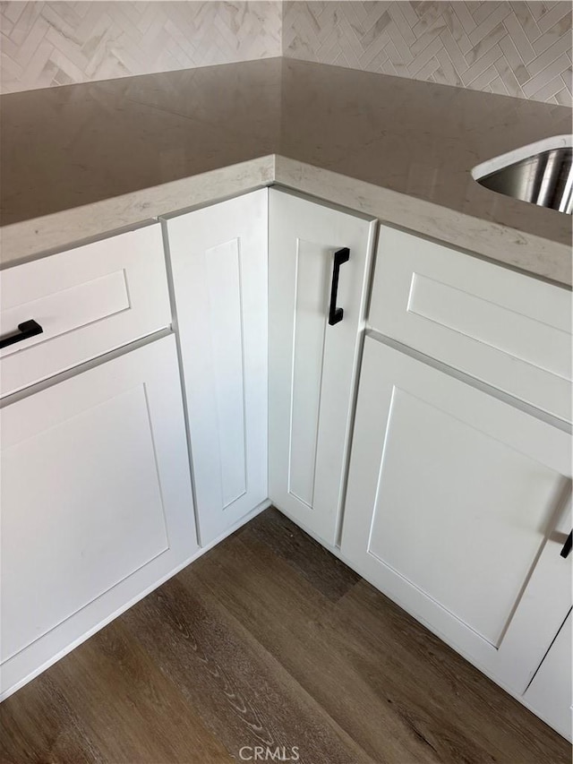 interior details with dark wood-style flooring, a sink, light stone countertops, and white cabinets