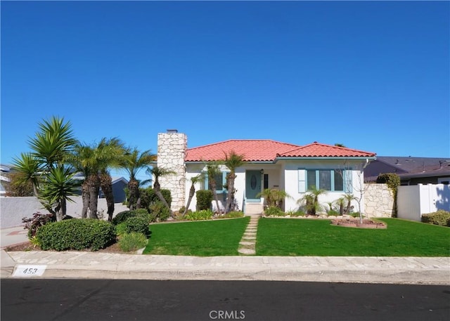 view of front of property featuring a tile roof, fence, stucco siding, a chimney, and a front yard