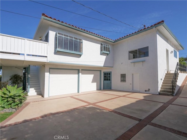 rear view of house with driveway, an attached garage, stairs, and stucco siding