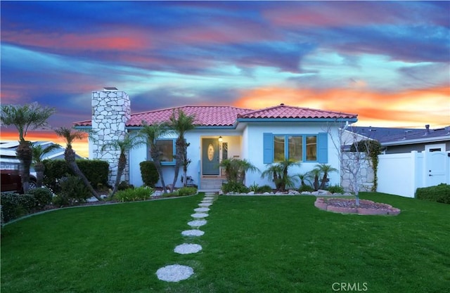 mediterranean / spanish house with fence, a tiled roof, a front lawn, and stucco siding