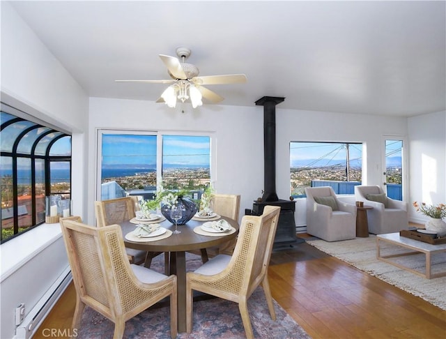 dining room featuring a baseboard heating unit, ceiling fan, hardwood / wood-style floors, and a wood stove