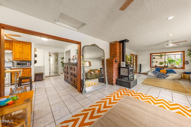 living area with light tile patterned floors, attic access, a wood stove, ceiling fan, and a textured ceiling