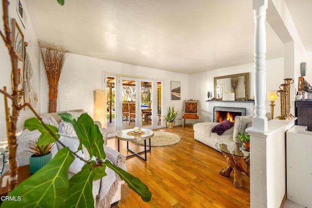 living area featuring wood finished floors, visible vents, decorative columns, a fireplace, and french doors