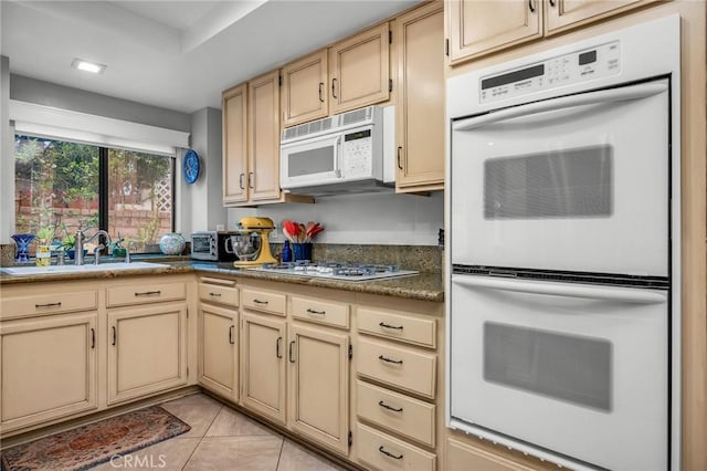 kitchen with white appliances, light tile patterned floors, dark countertops, cream cabinets, and a sink