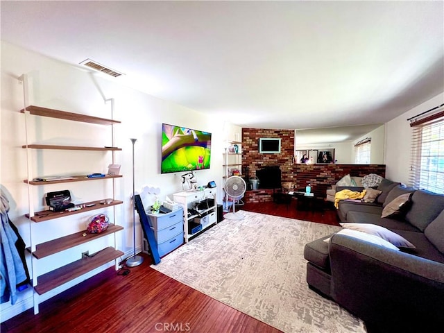 living room with a brick fireplace, visible vents, and dark wood finished floors