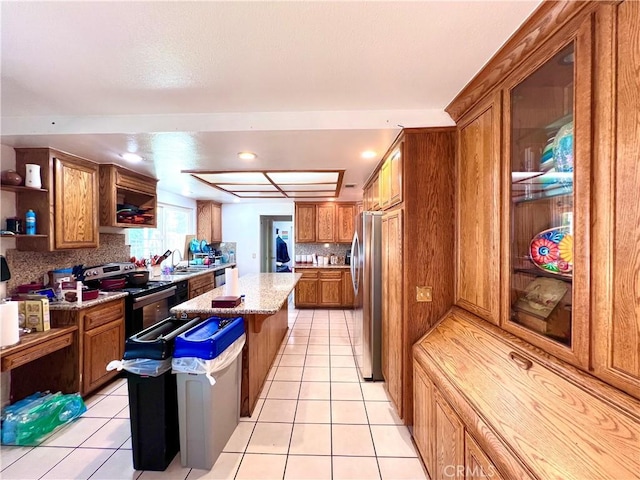 kitchen with stainless steel appliances, brown cabinetry, a kitchen island, and light tile patterned floors