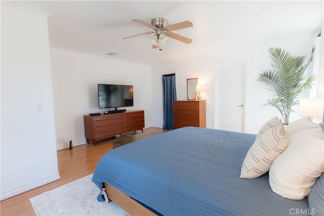 bedroom with a ceiling fan, visible vents, baseboards, and wood finished floors