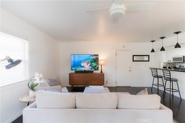 living area featuring a ceiling fan, dark wood-type flooring, and baseboards