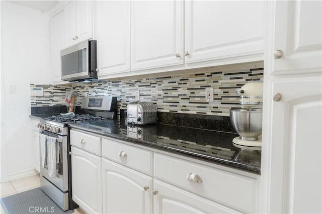 kitchen featuring light tile patterned flooring, stainless steel appliances, white cabinetry, dark stone counters, and tasteful backsplash