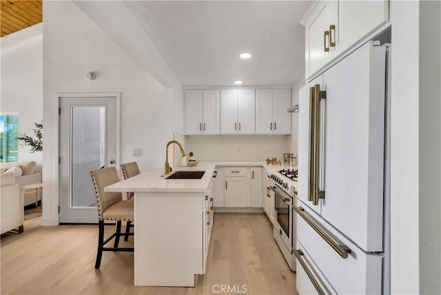 kitchen with a kitchen breakfast bar, high quality appliances, a sink, light wood-style floors, and recessed lighting