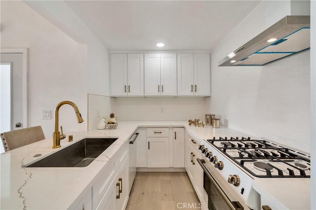 kitchen featuring a sink, white cabinetry, range with gas stovetop, wall chimney range hood, and light stone countertops