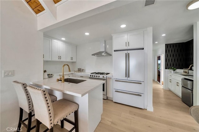 kitchen with high end fridge, a sink, gas stove, wall chimney exhaust hood, and visible vents