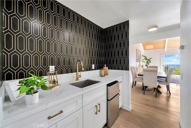 kitchen featuring freestanding refrigerator, light wood-style floors, white cabinets, light stone counters, and a sink