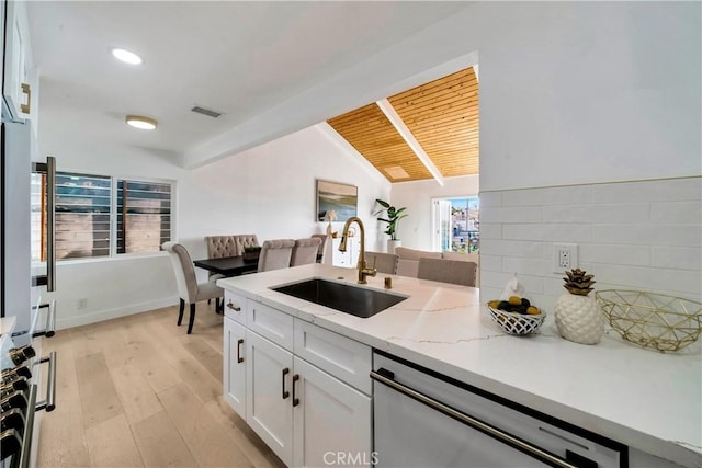 kitchen featuring white cabinets, dishwashing machine, vaulted ceiling with beams, light wood-style floors, and a sink