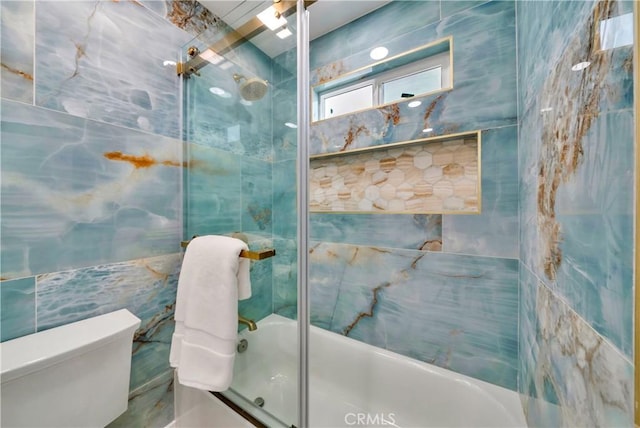 bathroom with bath / shower combo with glass door, toilet, and tile walls