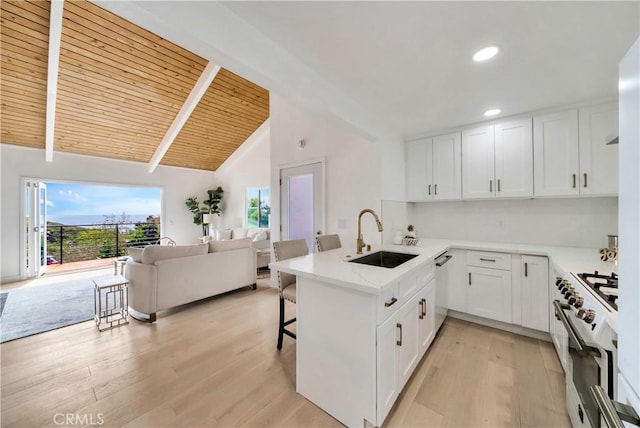 kitchen featuring vaulted ceiling with beams, a peninsula, a breakfast bar, a sink, and appliances with stainless steel finishes