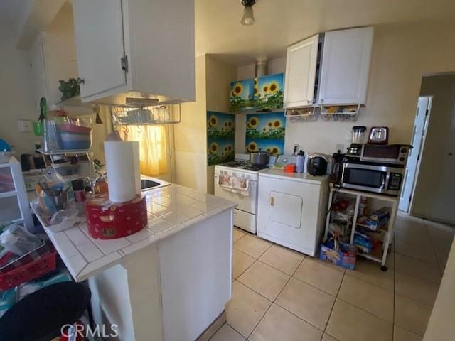 kitchen with white gas range, stainless steel microwave, white cabinetry, light tile patterned floors, and tile counters