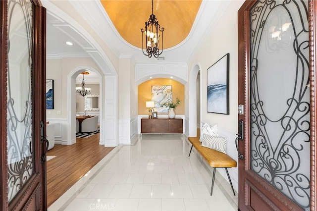 foyer with light tile patterned floors, arched walkways, ornamental molding, a decorative wall, and a notable chandelier