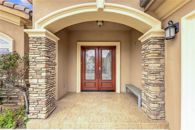 doorway to property featuring stone siding, french doors, and stucco siding