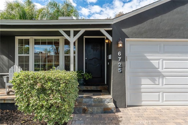 view of exterior entry with an attached garage and stucco siding