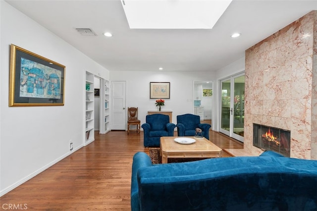 living area with a skylight, recessed lighting, visible vents, a tiled fireplace, and wood finished floors