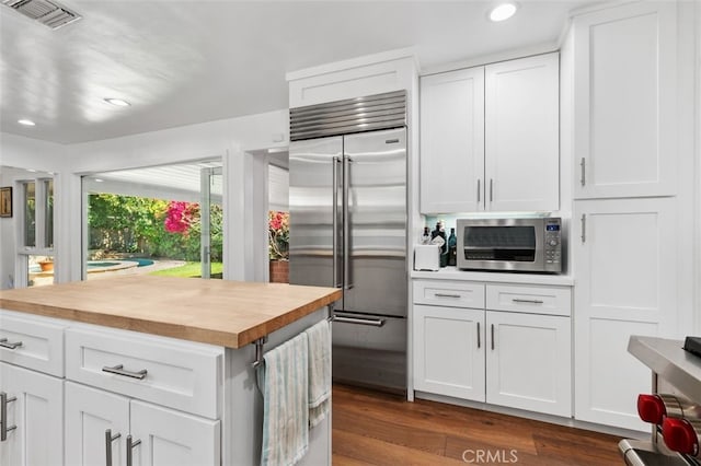 kitchen featuring dark wood-style floors, visible vents, appliances with stainless steel finishes, white cabinetry, and wood counters