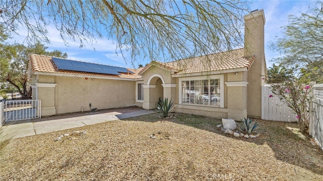 rear view of property with fence, a chimney, roof mounted solar panels, and stucco siding