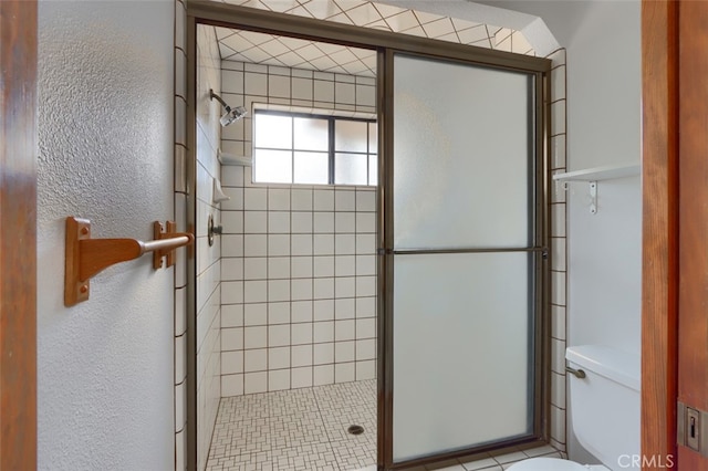 bathroom featuring a textured wall, a shower stall, and toilet