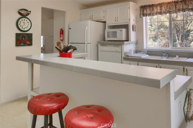 kitchen featuring white appliances, white cabinets, a sink, and light countertops